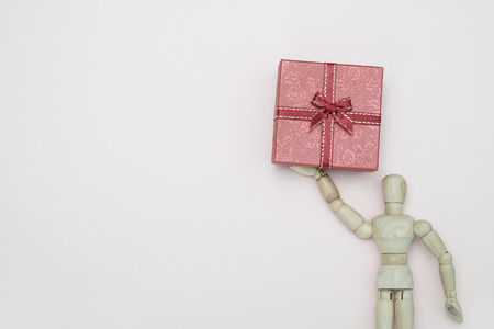 Wooden dummy holding a gift box  on pink background with copy space for write and valentine and new year concept.の写真素材