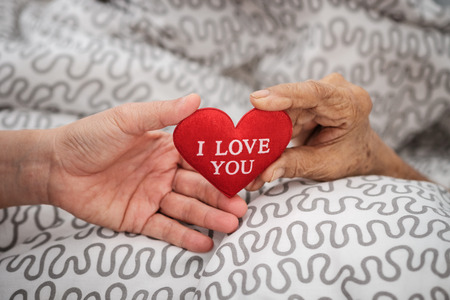 Hands of an elderly woman holding a red heart. Love in family concept.の写真素材