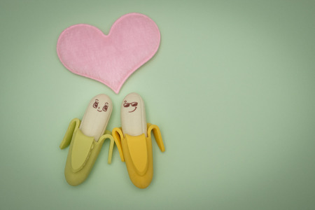 Two rubber banana and heart-shape pillow on green background, valentine concept.の写真素材