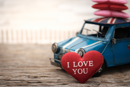 Red pillow heart shape and car toy on wooden background with space to write. Valentine concept, Vintage tone, AF point selection.の写真素材