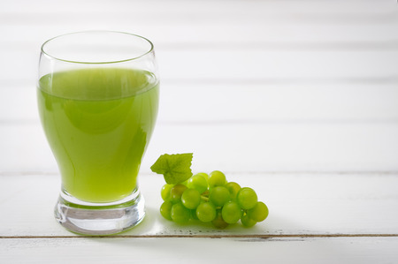 A glass of grape juice and bunch of green grapes on white wooden background, Selective focus.の写真素材