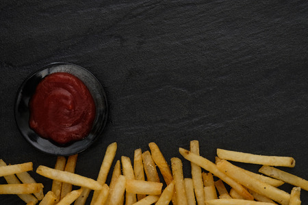 Fresh fried french fries with ketchup on black background. Choose focus point.