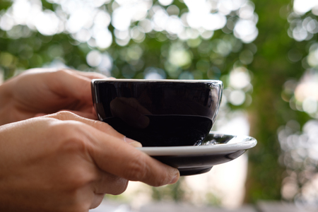 Hand is holding a glass of black ceramic in bokeh background.の写真素材