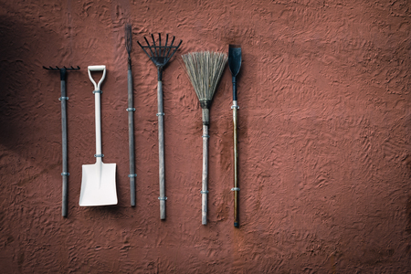 Broom, shovel, rake,spade hang on orange cement wall,Garden equipment groundworks hang on the red wallの写真素材