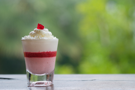 Strawberry mousse cake in a small glass placed on a wooden table in bokeh background with copy space.の写真素材