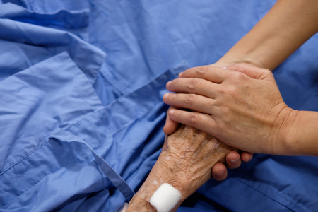 The hand of the woman is holding mother's hand that sleeping in the hospital bed.の写真素材