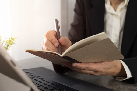 Businessmen holding a pen and writing a note in a notebook in office.の写真素材