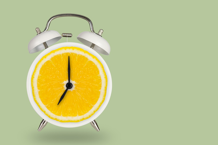 Creative fresh lime slice alarm clock on pastel green background, idea concept with copy space.の写真素材