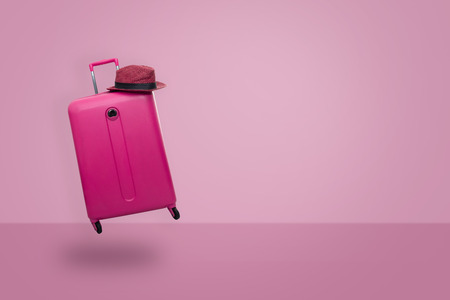 Pink suitcase with hat  on pastel pink background. travel concept. minimal style.の写真素材