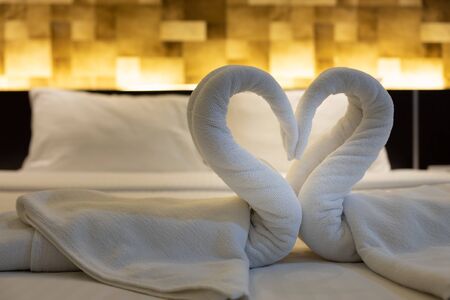 Close-up folded swans bird of fresh white bath towels on the bed sheet in the hotel.の写真素材
