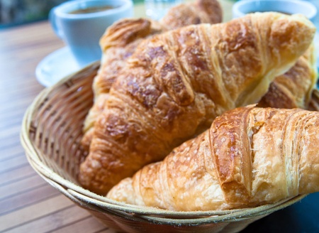 Breakfast with coffee and croissants in a basket on tableの写真素材