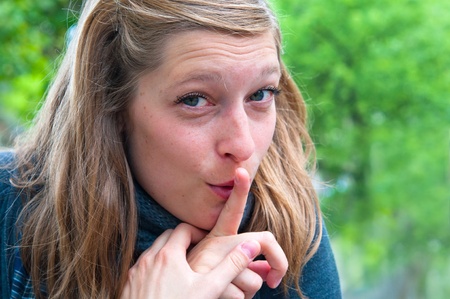 Outdoor portrait of a beautiful young woman hushing の写真素材