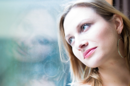 Beautiful woman standing by a window looking outsideの写真素材