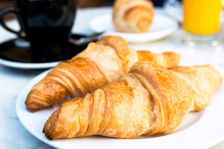 Breakfast with coffee and croissants in a basket on tableの写真素材