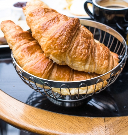 Breakfast with coffee and croissants in a basket on tableの写真素材