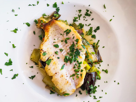 Grilled fish with zucchini and vegetables in white plate ready to be servedの写真素材