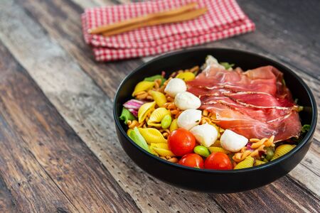 Salad made with cooked pasta, mixed green salads, cherry tomatoes, Mozzarella cheese and smoked ham served with accompanimentの写真素材