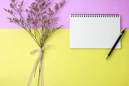 Blank notebook and pencil on pink and yellow background with a bunch of dry flower. Top view, flat lay.の写真素材