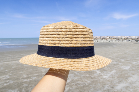 Woman hand holding beach hat with beach background.の写真素材