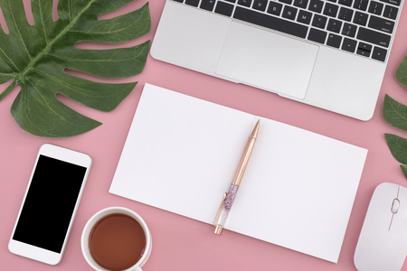 Flat lay of laptop, notebook, smart phone, pen, mouse , tea and Philodendron leaves on pastel background. Top view.の写真素材