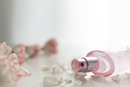 A Pink perfume bottle with pink and white carnation flowers and petals.