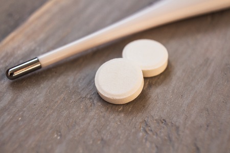 a thermometer with white pills on wooden background