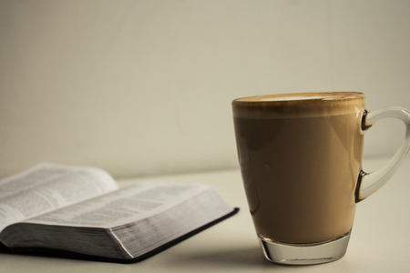 open bible and a cup of cappuccino with milk heart on white backgroundの写真素材