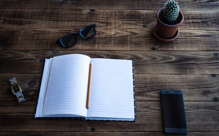 a notebook and pencil and cactus and watch phone glasses on wooden bacgroundの写真素材