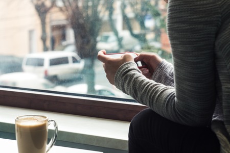 a girl hold a phone near the window wit coffeeの写真素材