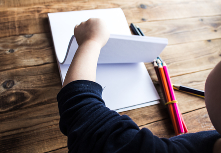 little boy draws on white paper with colored pencilsの写真素材