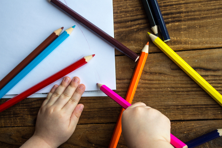 little boy draws on white paper with colored pencilsの写真素材