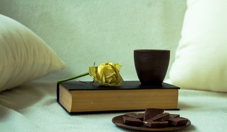 a cup on the book with rose and chocolate on the couchの写真素材