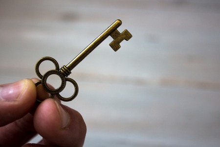 ancient key in the fingers of a man on wooden backgroundの写真素材