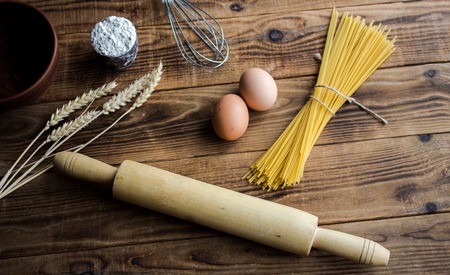 a spaghetti and flour and eggs with kitchenware on wooden background