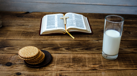 open bible cookies and milk on wooden background