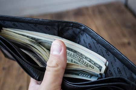 a wallet with money in a hand on a wooden background