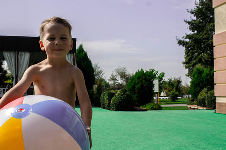 a litlle boy holds the ball near the poolの写真素材