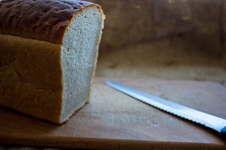 a homemade bread on a wooden plank with a knife in the background of burlapの写真素材