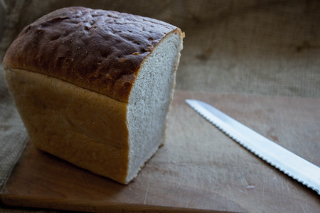 a homemade bread on a wooden plank with a knife in the background of burlapの写真素材