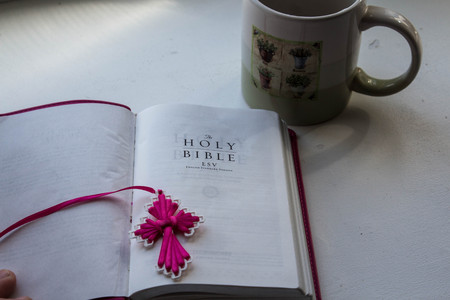 open bible with a cross with a cup of tea on a white background