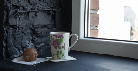 cup with tea and cupcake near the windowの写真素材