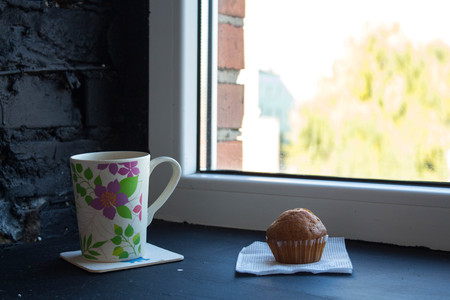 cup with tea and cupcake near the windowの写真素材