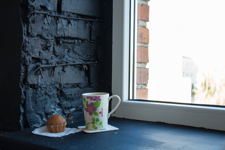 cup with tea and cupcake near the windowの写真素材
