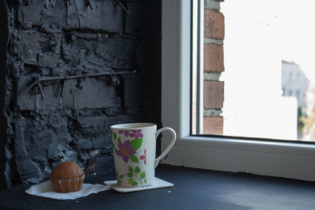 cup with tea and cupcake near the windowの写真素材