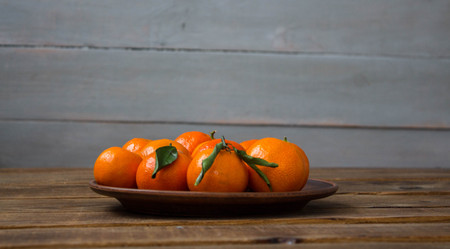 a ripe tasty tangerines on a plate on a wooden backgroundの写真素材
