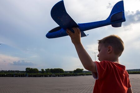 boy playing with a blue airplane in the street against a blue skyaの写真素材