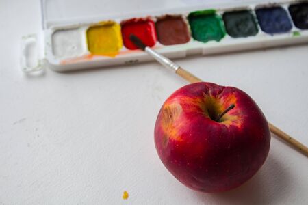 a red apple and watercolor paint and brush on white backgroundの写真素材