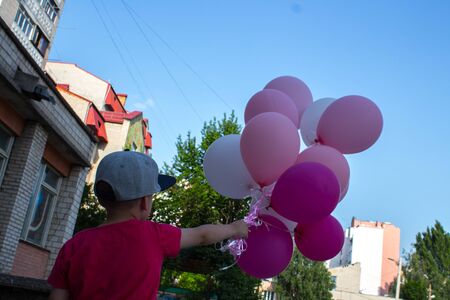 little boy in the yard holds in his hand a lot of colored balloonsの写真素材