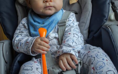 baby holds a spoon in his hands in the kitchenの写真素材