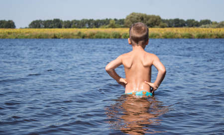 boy stands in the water against the background of a yellow fieldの写真素材